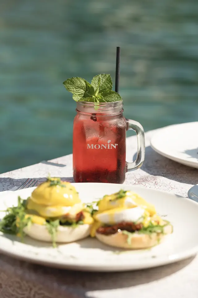 Red berry drink and eggs Benedict beside the bay